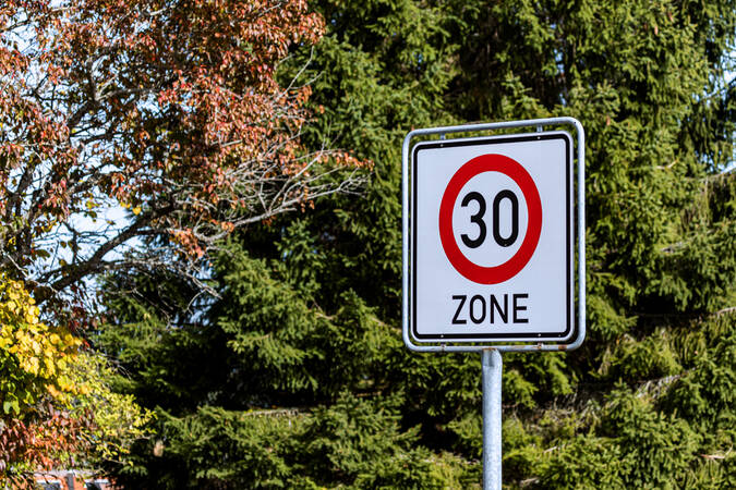 Ein Verkehrsschild, das auf den Beginn einer Tempo-30-Zone hinweist. Im Hintergrund steht eine grüne Tanne.